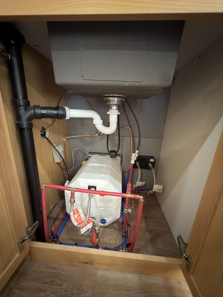 Van Niewkoop Camp #136: Drain plumbing and the 6-gallon propane water heater accessible beneath the kitchen sink.
