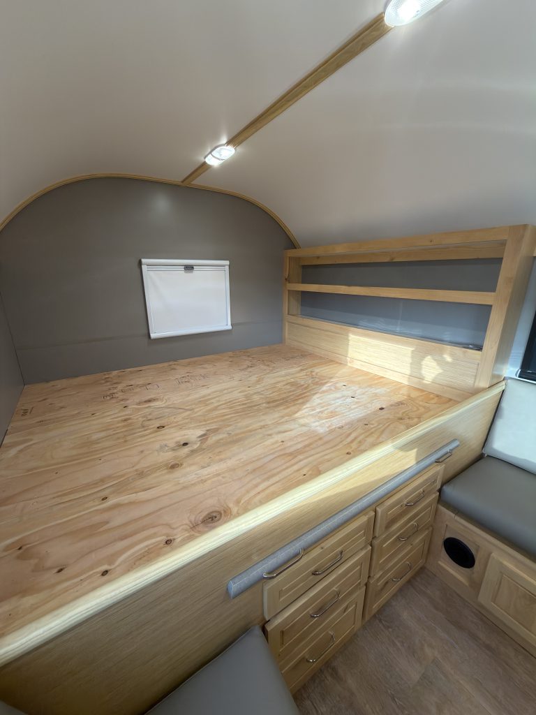 Van Niewkoop Camp #136: Raised east/west California king bed platform beneath a window with its blackout blind lowered.
