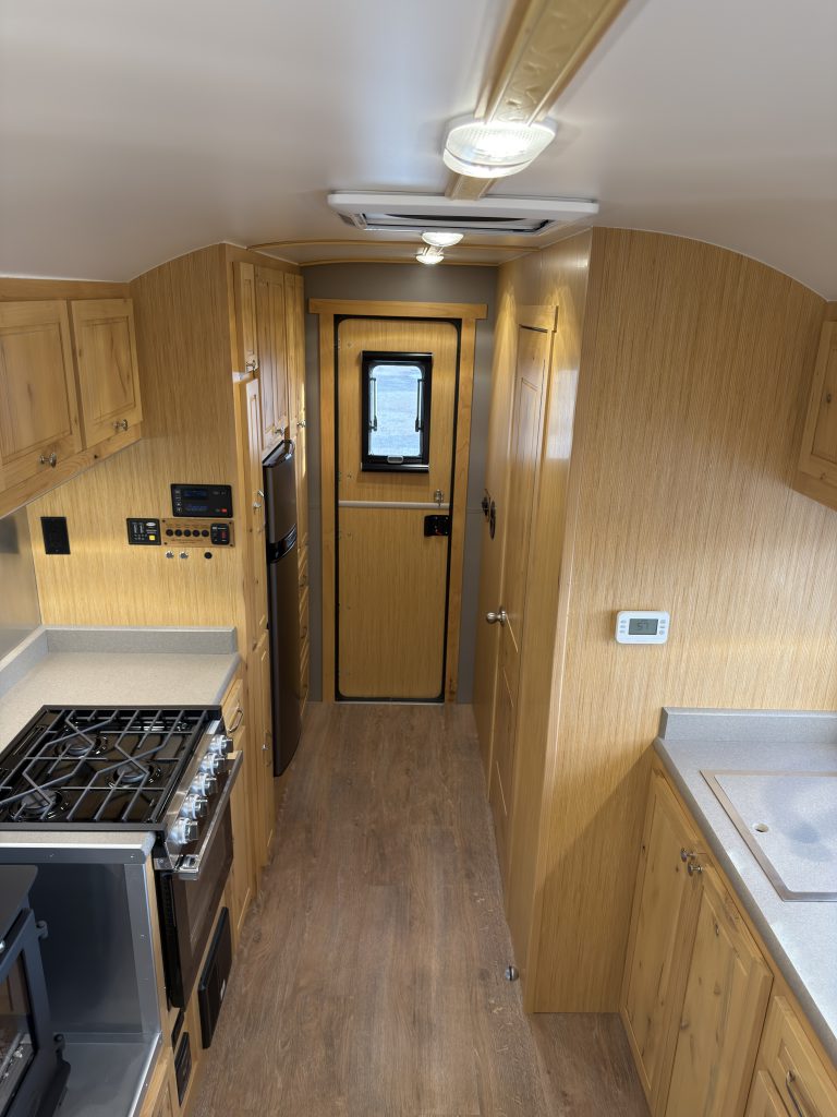 Wide interior view along the kitchen aisle toward the entry in Van Niewkoop Camp #136.
