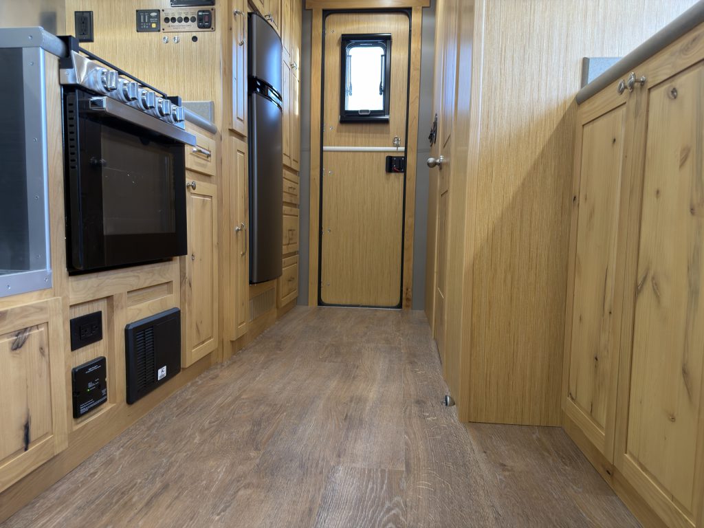 Van Niewkoop Camp #136: Low view down the luxury vinyl plank aisle beside the GE range and wood storage cabinets.