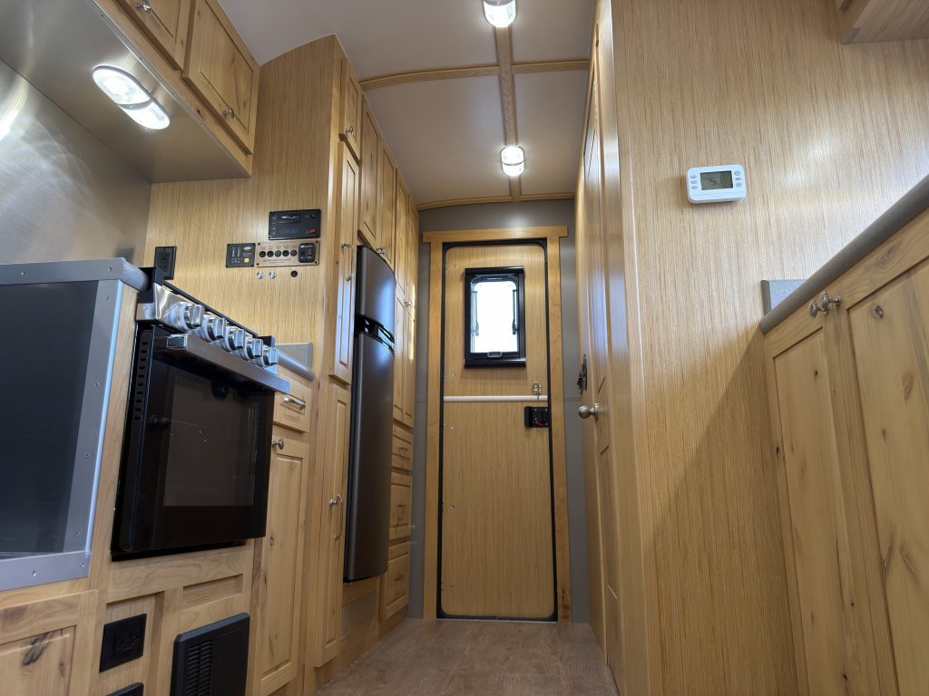 Van Niewkoop Camp #136: Interior aisle beside the GE range, compact wood stove, and hardwood cabinetry.