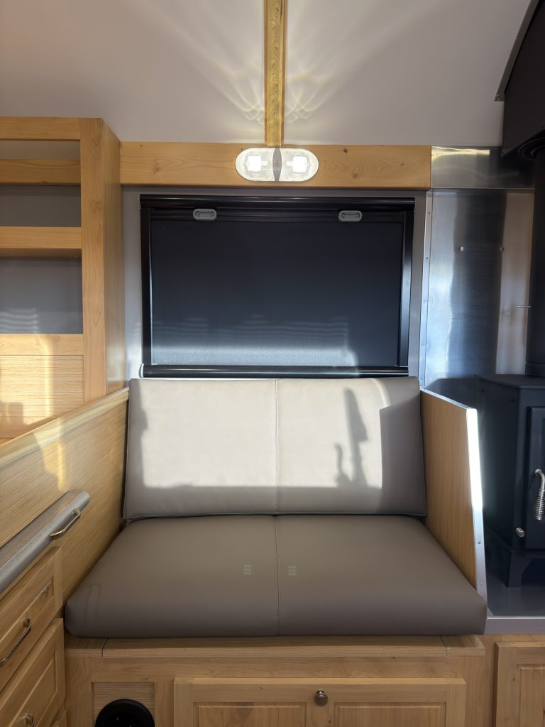 Van Niewkoop Camp #136: Upholstered angled side bench beneath a window with its blackout blind lowered.