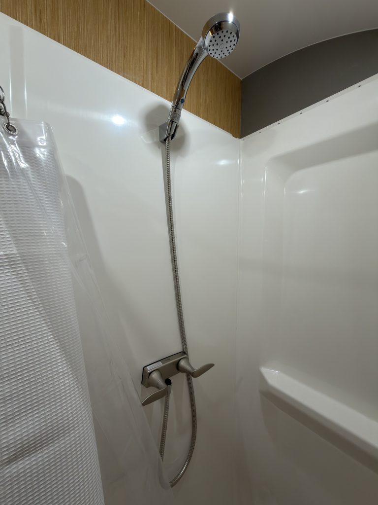 Van Niewkoop Camp #136: Stainless steel shower fixtures with a shower head, mixer, hose, and molded wall shelves.