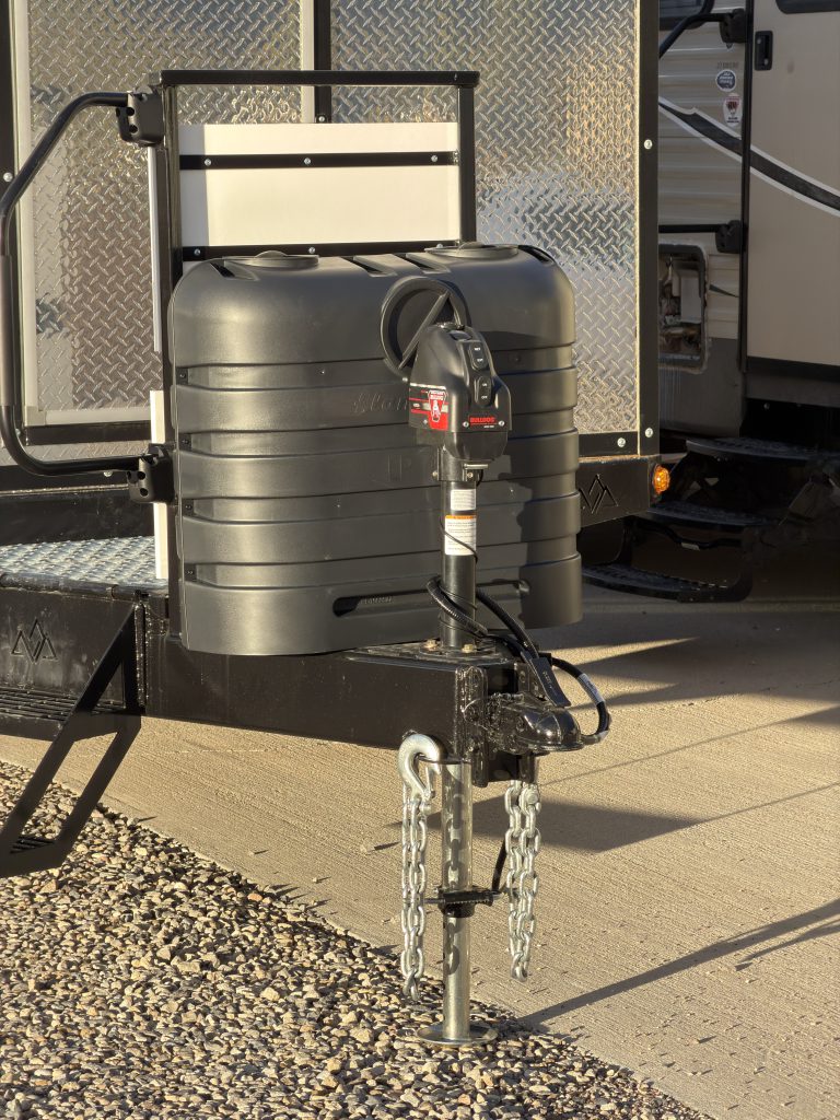Van Niewkoop Camp #136: Quick-access propane tank cover, Bulldog electric tongue jack, and hitch assembly in sunlight.