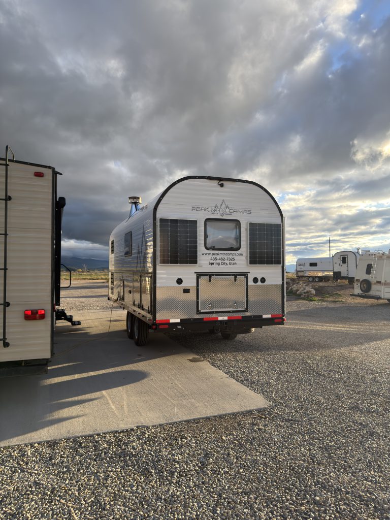 Distant rear view of the camp beside another trailer in Van Niewkoop Camp #136.