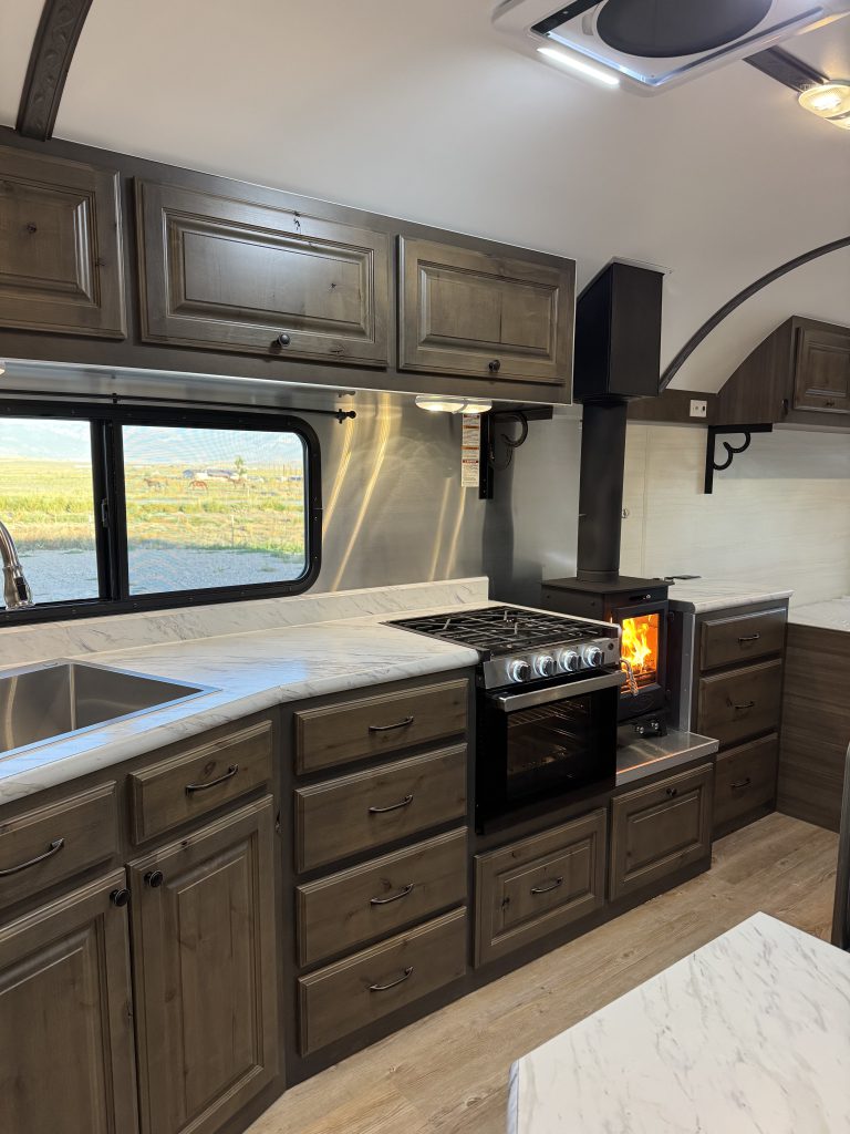 Kitchen with wood cabinetry, a stainless sink, range, and lit wood stove in Watson Camp #134.