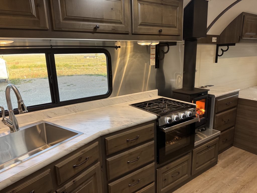 Kitchen counter beneath a window, with a sink, range, and wood stove in Watson Camp #134.