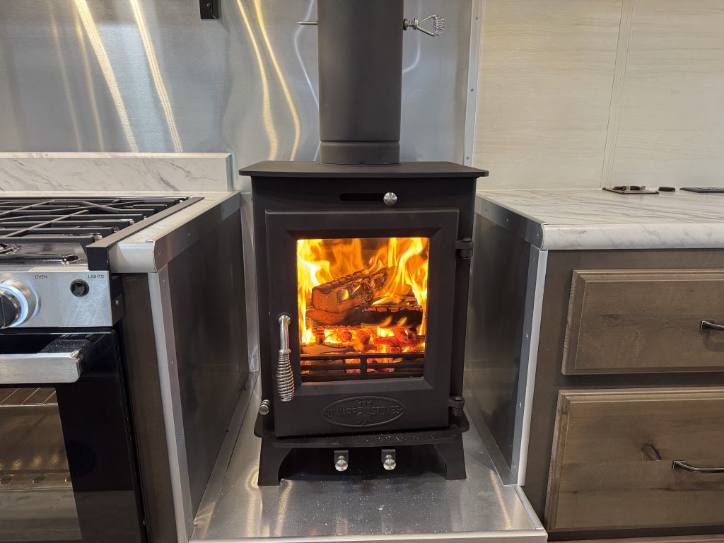 Wood stove with a visible flame, metal wall surround, and hearth in Watson Camp #134.