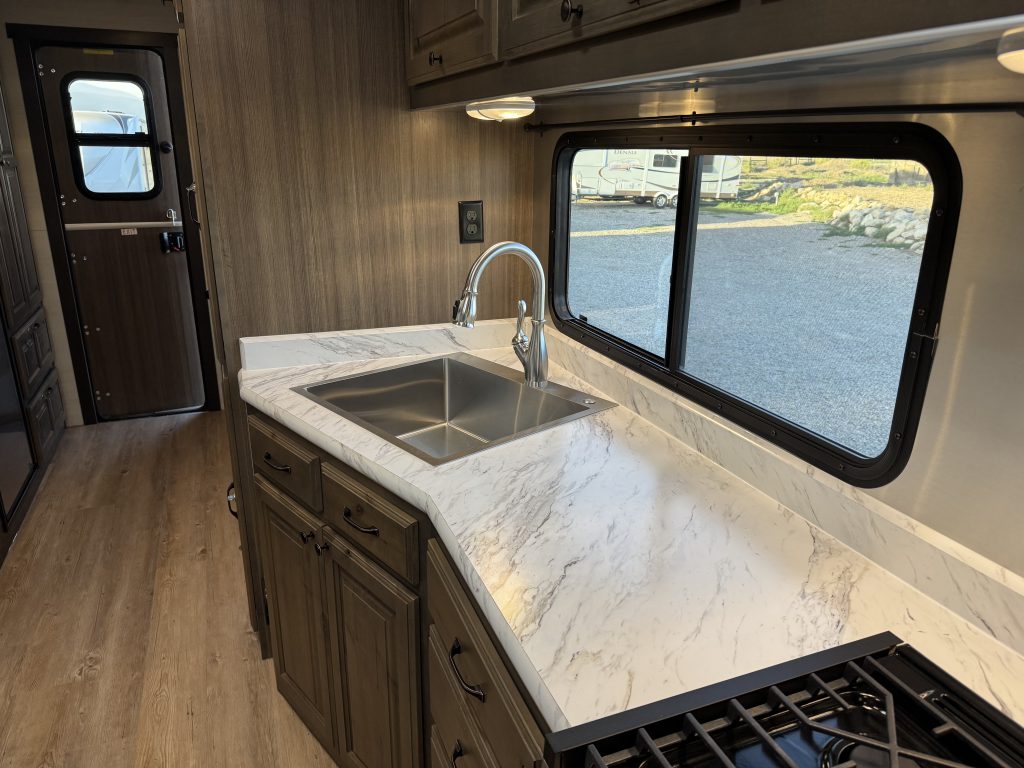 Stainless sink and curved faucet set into a light countertop beneath a window in Watson Camp #134.