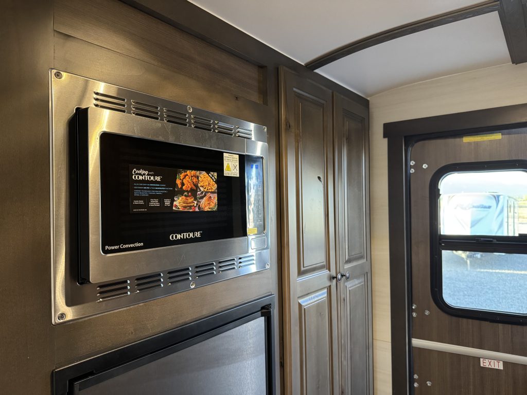 Stainless microwave above the refrigerator beside a tall cabinet and entry door in Watson Camp #134.