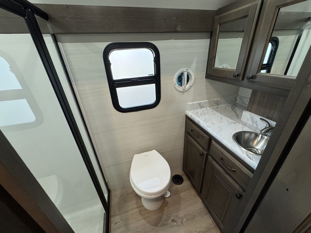 Bathroom with toilet, sink vanity, mirrored cabinets, window, and enclosed shower in Watson Camp #134.