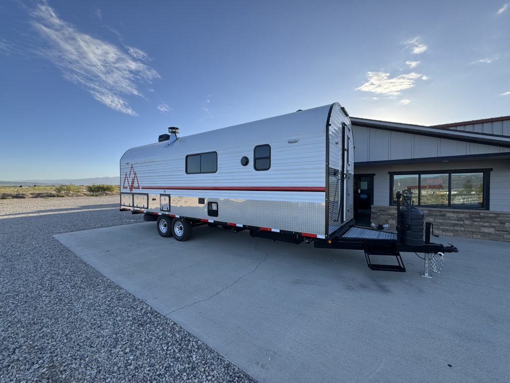 Entry-side exterior showing windows, tandem wheels, front steps, and trailer tongue in Watson Camp #134.