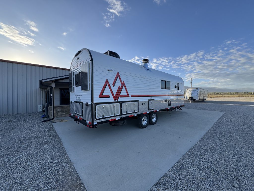 Rear corner view with a Peak graphic, side windows, tandem wheels, and dual rear solar panels in Watson Camp #134.