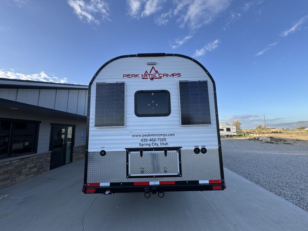 Straight rear view showing a center window, dual solar panels, and bumper in Watson Camp #134.