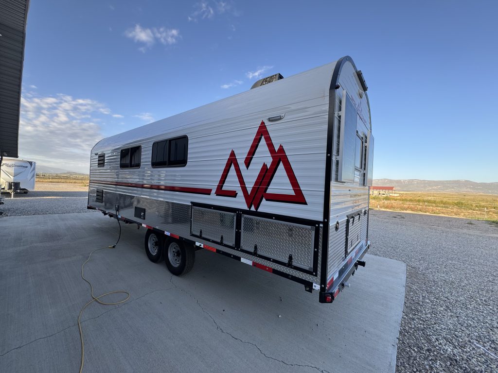 Rear corner and utility-side view with a Peak graphic, windows, and lower compartments in Watson Camp #134.