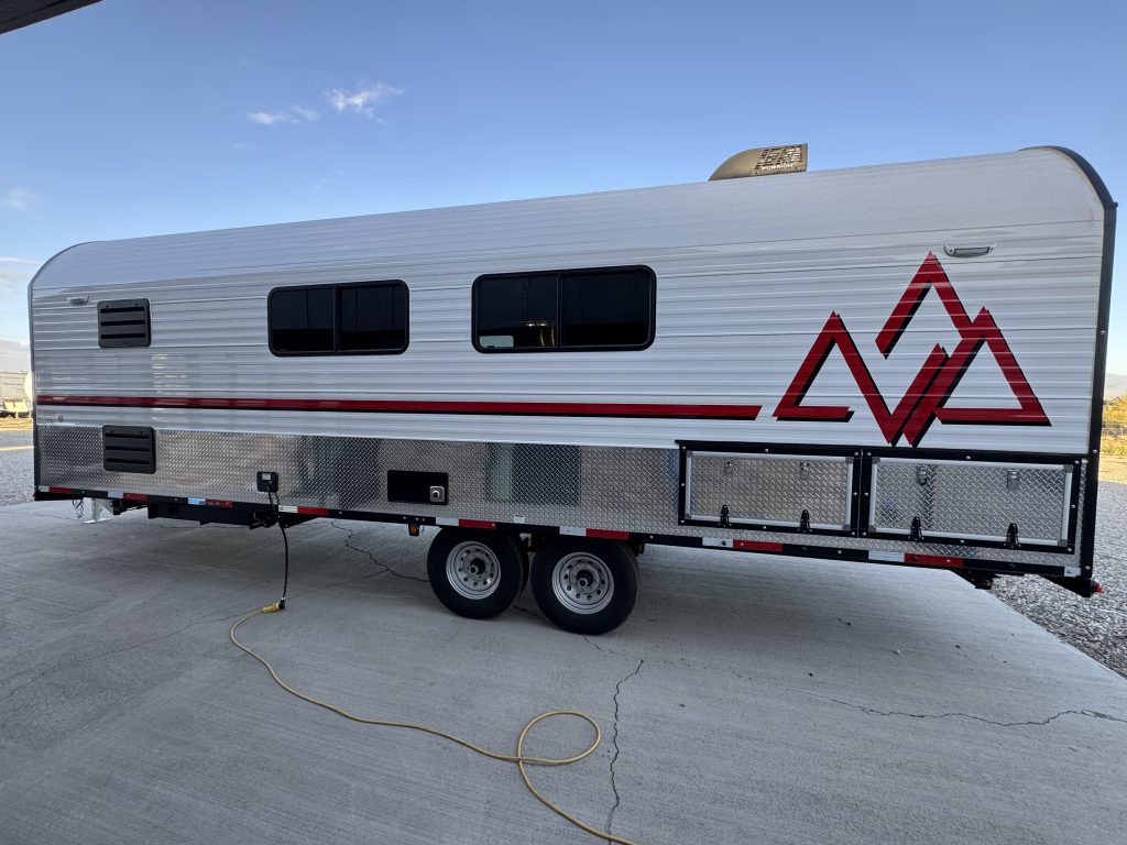 Utility-side exterior with windows, tandem wheels, a Peak graphic, and lower compartment doors in Watson Camp #134.