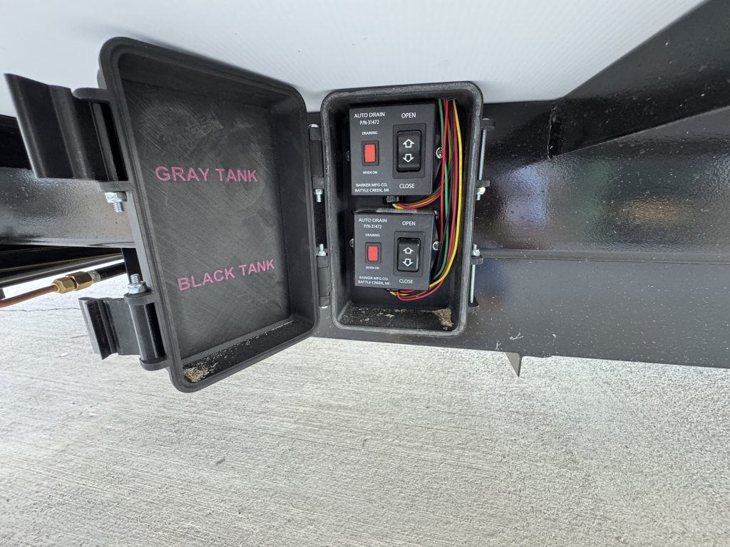 Open exterior compartment labeled gray tank and black tank, with two control panels and visible wiring in Watson Camp #134.