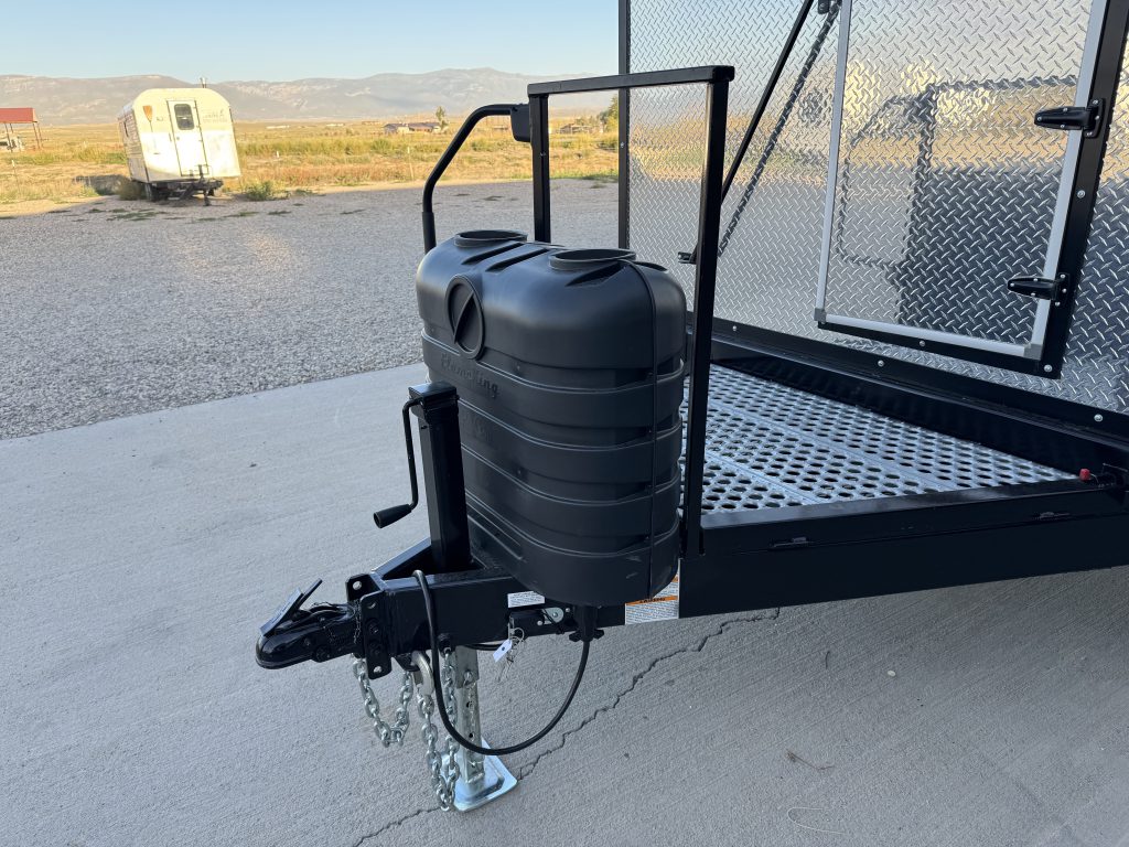 Trailer tongue with hitch coupler, safety chains, covered propane cylinders, and front platform in Watson Camp #134.