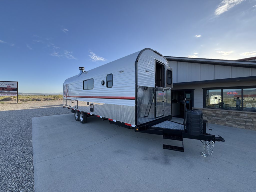 Angled entry-side view showing side windows, tandem wheels, open front door, and steps in Watson Camp #134.