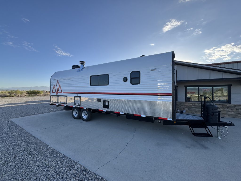Front corner view showing the long side wall, windows, tandem wheels, and entry steps in Watson Camp #134.