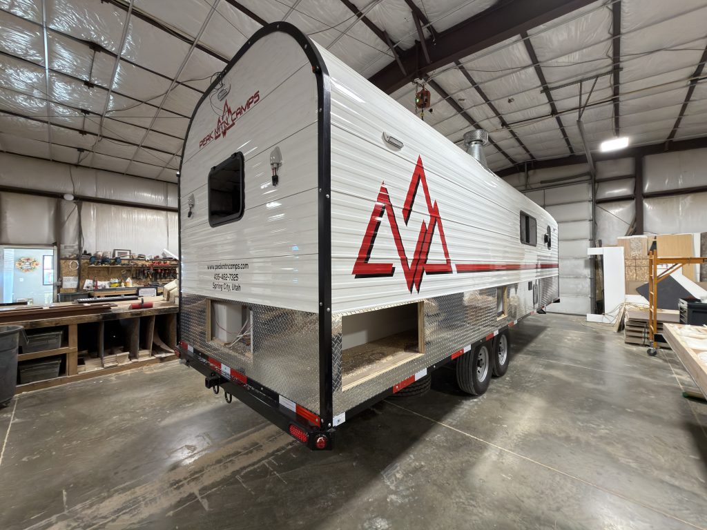 Wide rear roadside view inside the workshop, with red Peak graphics, tandem wheels, and open lower compartment bays in Watson Camp #134.