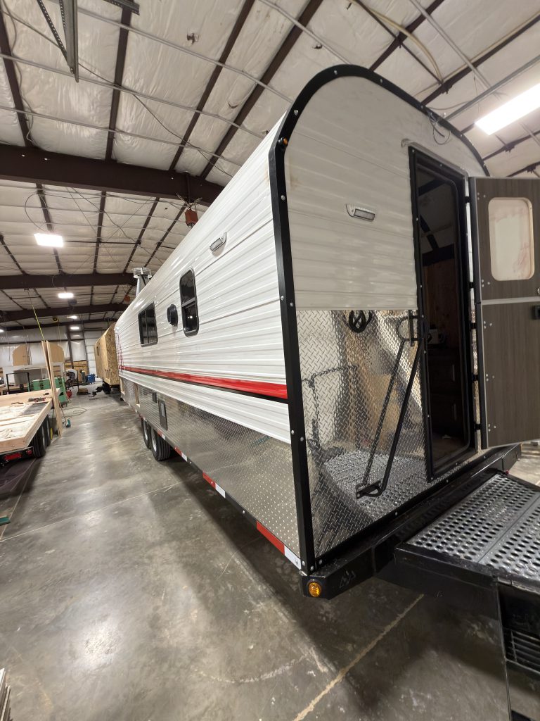 Front entry-side angle inside the workshop, showing the open entry door, handrails, side windows, and front platform in Watson Camp #134.
